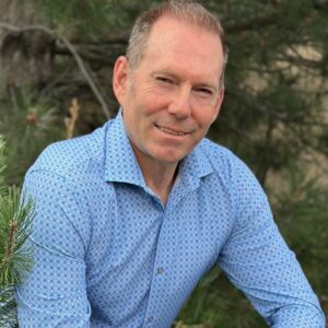 Image of Keven Winder from the waste up. He is next to a tree and smiling.