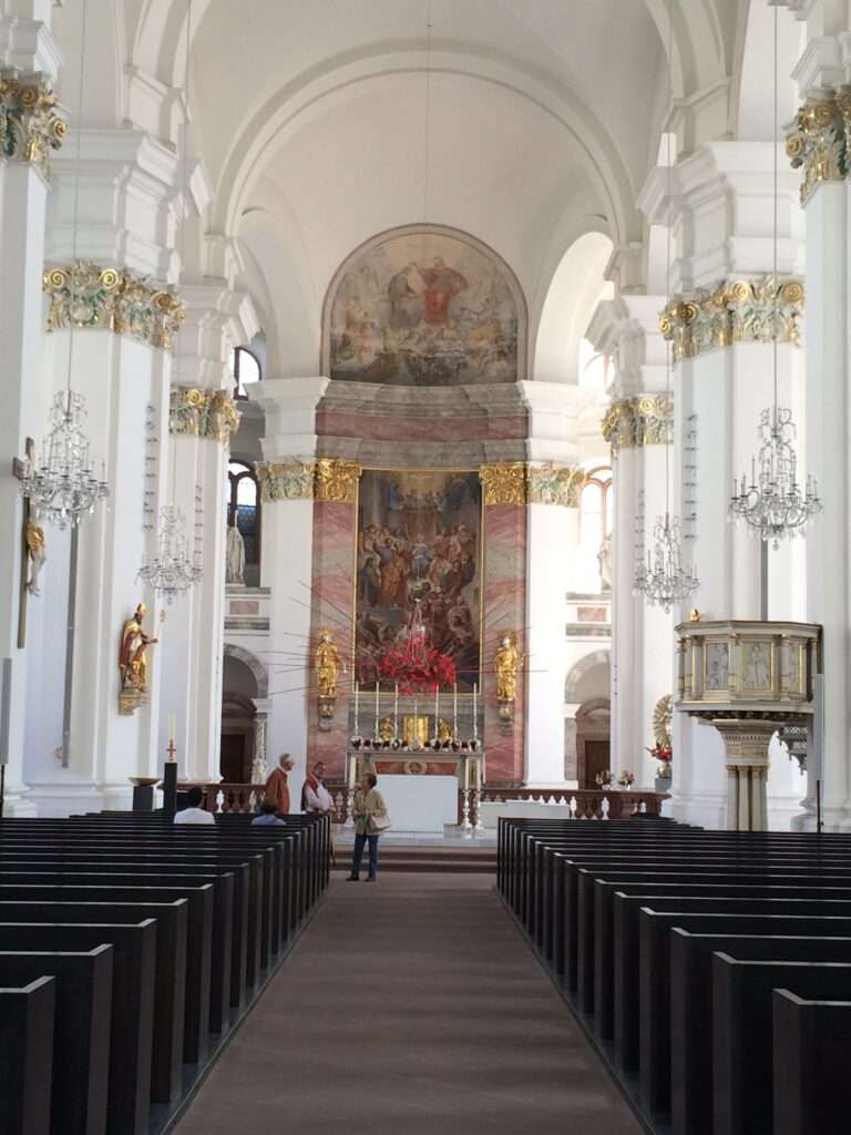 A picture of the interior of a beautiful Church. The view is looking down the center isle of the church with the very tall pillars and light shining in through the windows on the side.