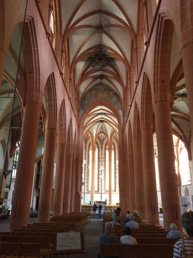 A picture of the interior of a beautiful Church. The view is looking down the center isle of the church with the very tall pillars and light shining in through the windows on the side.