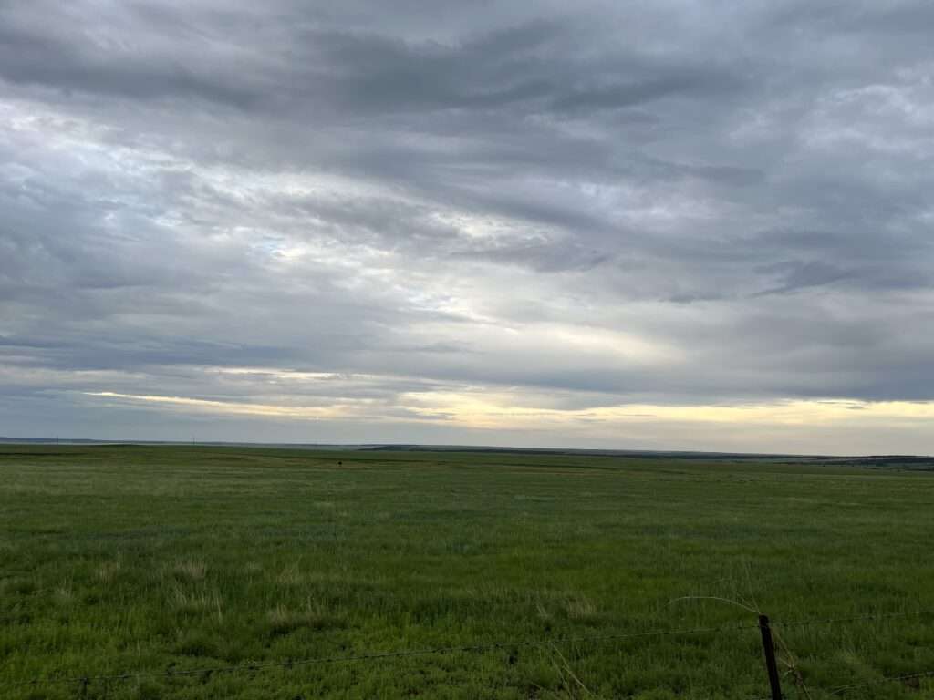 Sunrise on a cloudy day in the Spring time over a large grassy terrain with mountain vistas in the distance