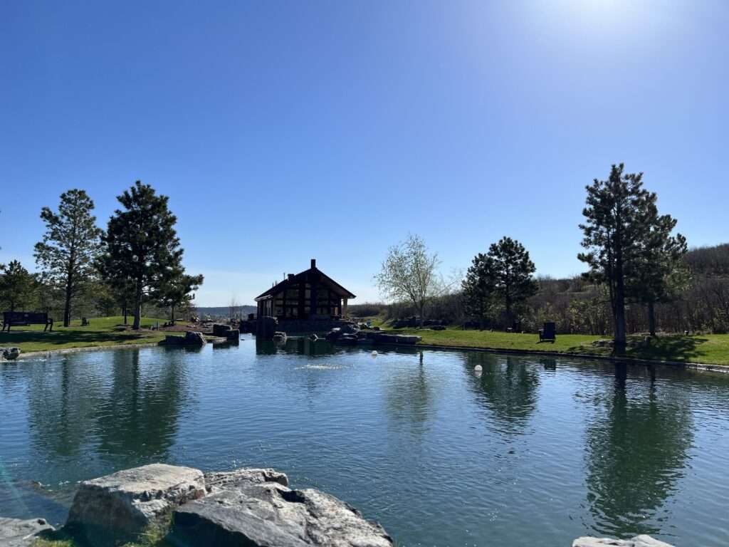 Image of the field house nestled against a reflective pond with pine trees surrounding it. Castle Rock, CO