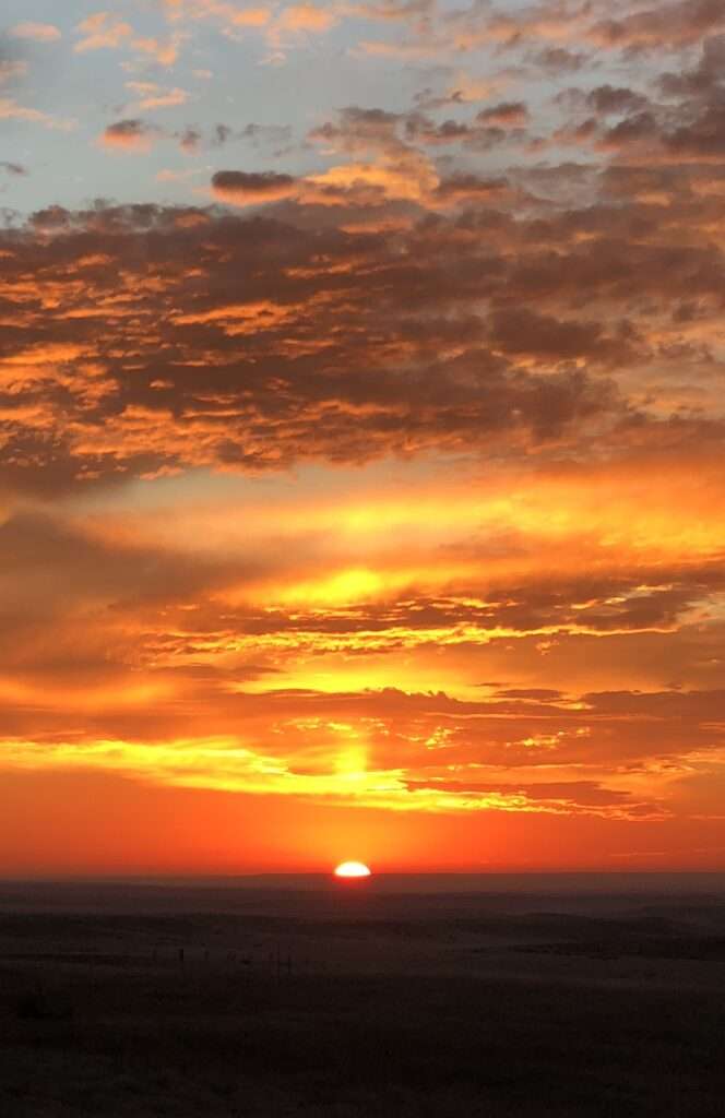 A picture of the sun emerging in a radiant cloudy sky over the rural plains of Wyoming.