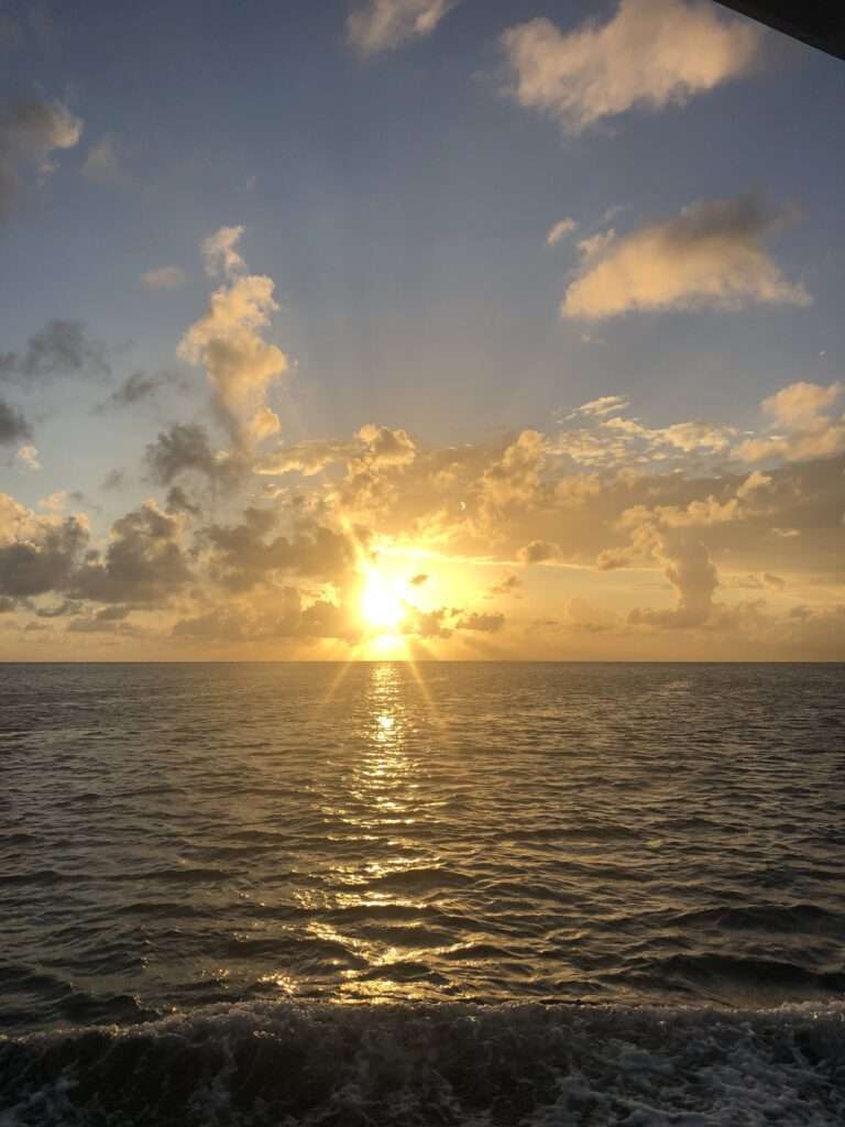 A picture of sunrise over the ocean with a cloudy sky