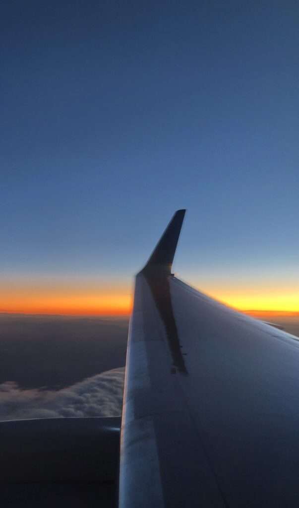 A picture of the break of sunrise from the seat of an airplane looking out over the wing